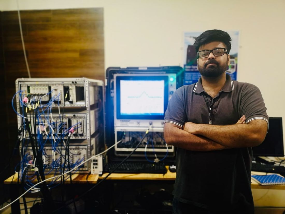 Standing beside a rack of signal-analysis instrumentation and oscilloscopes.